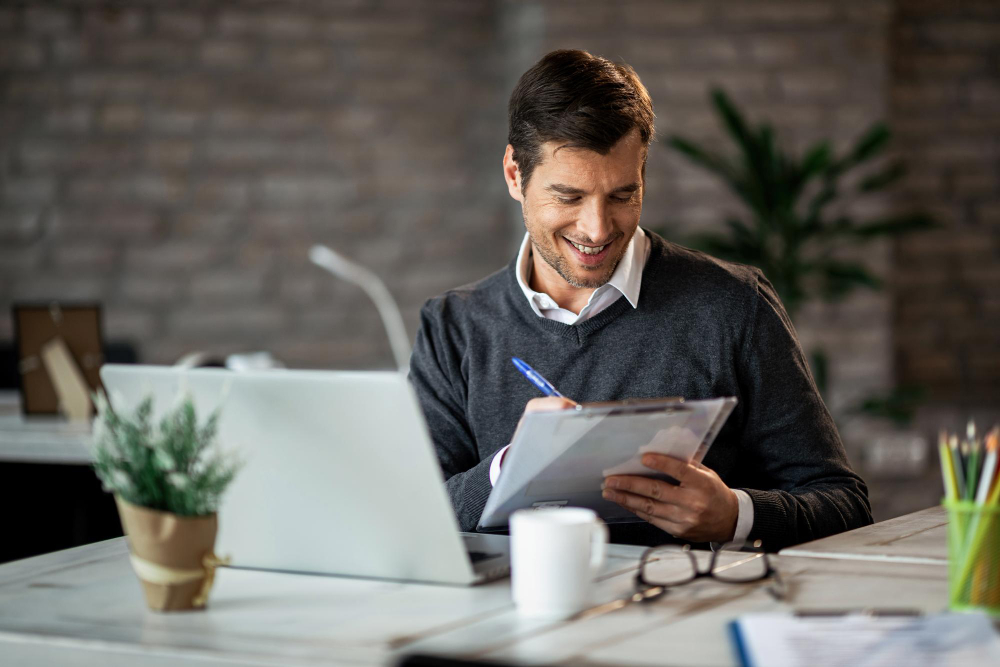 Um homem sentado na mesa analisando gráficos financeiros e sorrindo por todos estarem de acordo com as espectativas